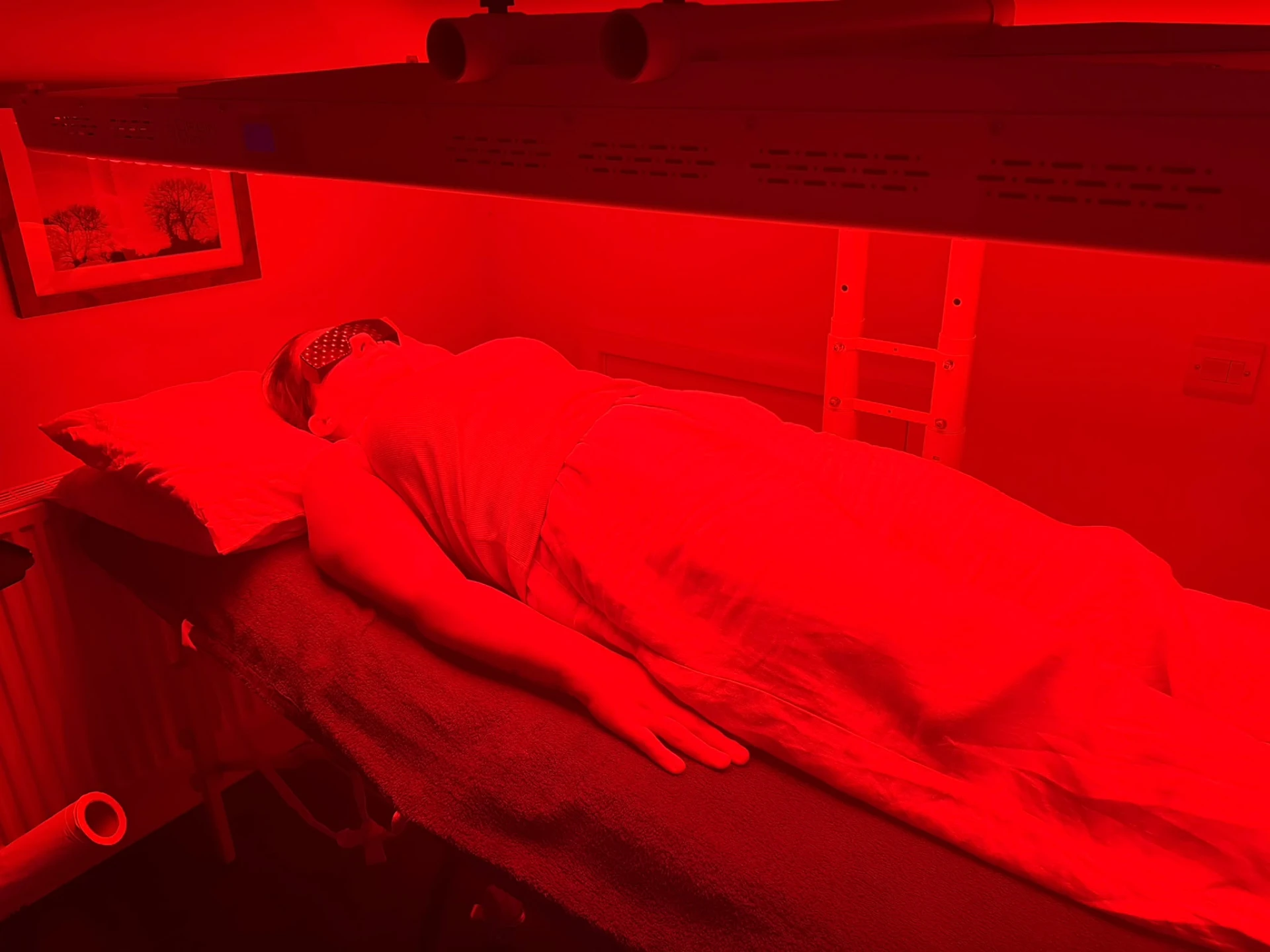 Client relaxing under red light therapy panels during a PEMF and red light session at RegenSuites Basingstoke